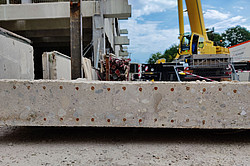 Photo: A yellow excavator is working on a construction site. In the foreground is a concrete wall.