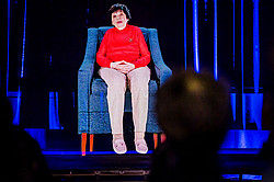 Photo: A holographic projection shows a person in a blue armchair against a dark background with blue light streaks.