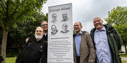 Four men are leaning against a stele that displays the name "EUnet Alley" as well as drawings of the heads of Dortmund’s Internet pioneers.
