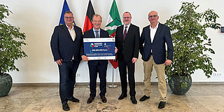 Four people with grant notification, flags in the background