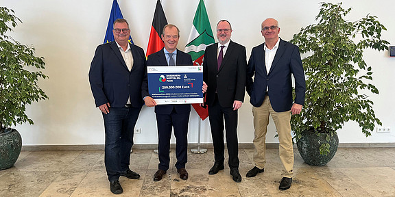 Four people with grant notification, flags in the background