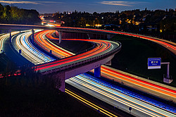 Nighttime photograph of a highway interchange in the Ruhr region; the taillights form red stripes, while the headlights form white stripes.