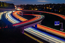 Nighttime photograph of a highway interchange in the Ruhr region; the taillights form red stripes, while the headlights form white stripes.