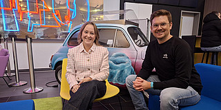 Foto: Michelle Twardzik und Dr. Thomas Seidensticker sitzen in auf einer blauen Couch und einem gelben Stuhl und lächeln in die Kamera.