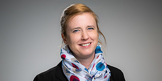 Portrait photo of Prof. Wiederkehr: Prof. Wiederkehr wears a patterned scarf and a black blazer. She smiles at the camera.