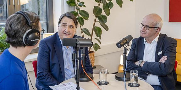 Recording situation for a podcast: Three men are sitting at a round table.