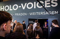 Photo: Several people stand in front of an entrance labeled “Access Holograms” beneath the large sign “HOLO-VOICES.”