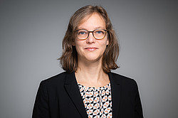 Portrait photo of Prof. Nele McElvany: Prof. McElvany is wearing a dark blazer and glasses. She stands in front of a gray background and smiles at the camera.