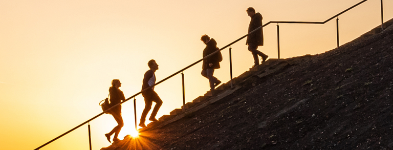 Side view of a slag heap, groups of people climbing up or down a staircase.