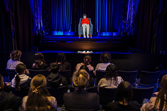 Photo taken in the screening room showing a school class from behind watching the hologram of a contemporary witness