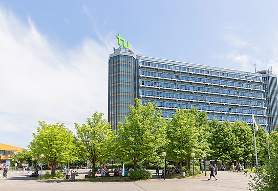 Photo: The north campus of TU Dortmund University in good weather. The photo shows the Math Tower with the TU logo and green trees.
