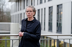 Portrait photo of Christina Lechtermann: Prof. Lechtermann is wearing dark clothing and leaning against a railing. A modern white building can be seen in the background.