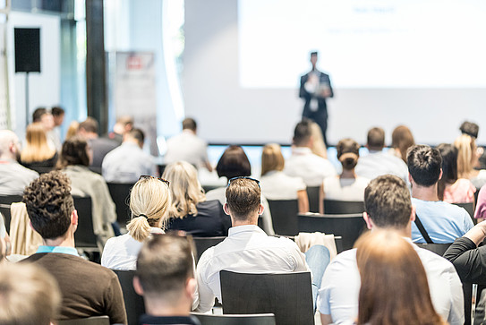 Rear view of people listening to a person speaking in the background