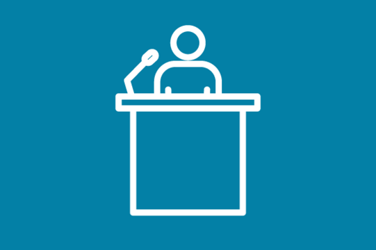 White icon on blue background: Person with microphone at lectern