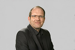 Portrait photo of Prof. Greiving: Prof. Greiving stands in front of a light gray background wearing a dark suit.