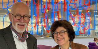 Foto: Prof. Weiler und Prof. Havenith-Newen lächeln mit Kafeetassen in der Hand in die Kamera.