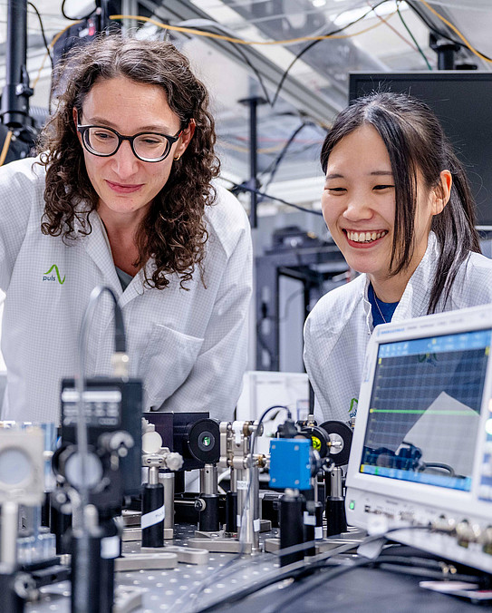 Two researchers examine an experimental setup with various devices in front of them.n mit verschiedenen Apparaturen
