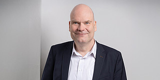 Porträtfoto von Dr. Jan-Martin Wiarda vor grauem Hintergrund. Dr. Wiarda trägt einen dunklen Anzug.