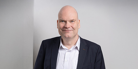 Porträtfoto von Dr. Jan-Martin Wiarda vor grauem Hintergrund. Dr. Wiarda trägt einen dunklen Anzug.