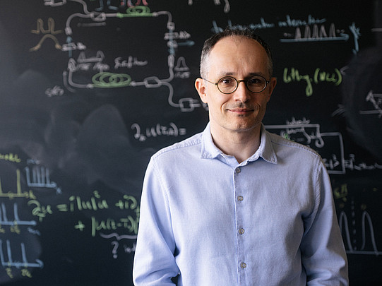 Portrait of Ömer Ilday in front of a blackboard covered with mathematical equations.
