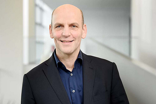 Portrit photo of Prof. Benjamin List: Prof. List is wearing a blue shirt and dark suit. He is smiling at the camera.