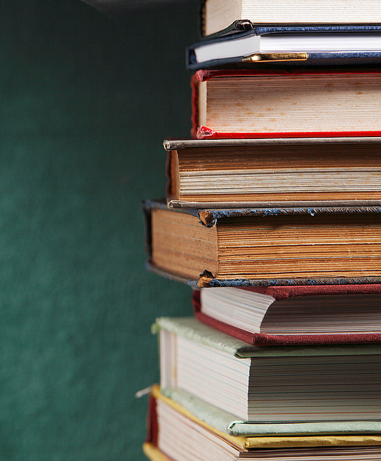 A pile of old, hardcovered books in front of a dark green background.