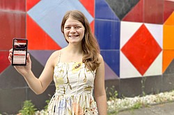 Photo: Elisabeth Jacobson stands in front of a work of art and holds up a smartphone displaying the Artventure app.