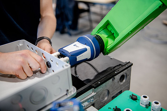 A person, of whom only the right hand and left arm are visible, is adjusting something on a robotic arm.
