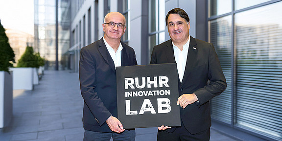 Foto: Prof. Martin Paul, Rektor der Ruhr-Universität Bochum, und Prof. Manfred Bayer, Rektor der TU Dortmund, mit dem Logo des „Ruhr Innovation Lab“.