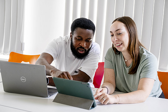 Photo: Two students sitting at a table looking at a laptop.