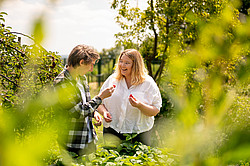 Foto: Zwei Studierende stehen im Campusgarten und probieren selbstgeerntete Erdbeeren.