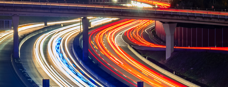 Nighttime photograph of a highway interchange in the Ruhr region; the taillights form red stripes, while the headlights form white stripes.