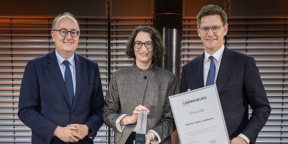 Photo: Three people are visible in the photo. A woman is receiving an award. 