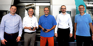Photo: Five people stand in front of a large machine in a workshop.