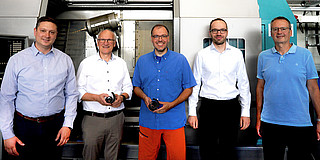  Foto: Fünf Personen stehen in einer Werkstatt vor einer großen Maschine.