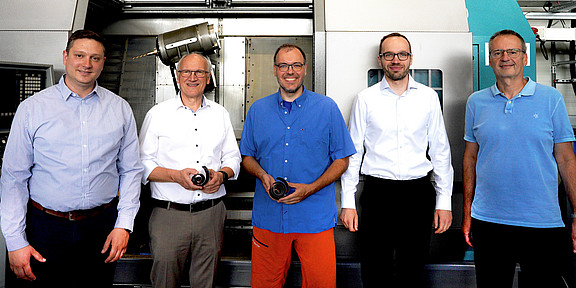Foto: Fünf Personen stehen in einer Werkstatt vor einer großen Maschine.