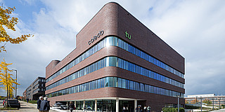 Photo: An exterior view of the CALEDO research building. CALEDO is a brick-style building with large windows and rounded edges.
