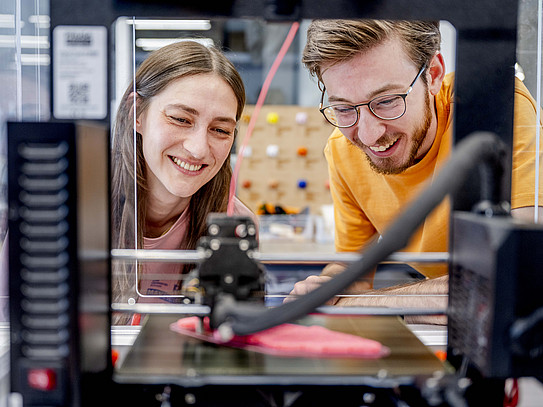 Photo: Two people look into a transparent device that processes material.