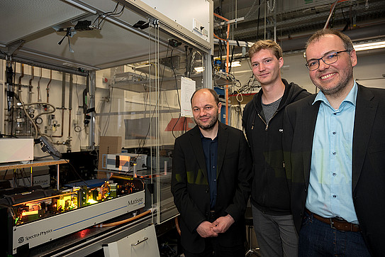 Photo: Three physicists standing next to a laser experiment