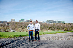 Photo: Two men in shirts are standing on a path. Behind them is a field and the campus of Ruhr University Bochum.