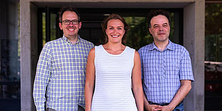 A group of three people is smiling at the camera