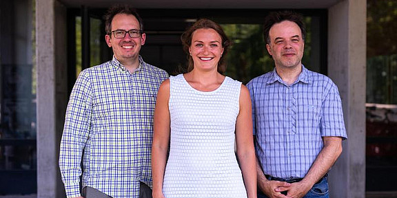 A group of three people is smiling at the camera