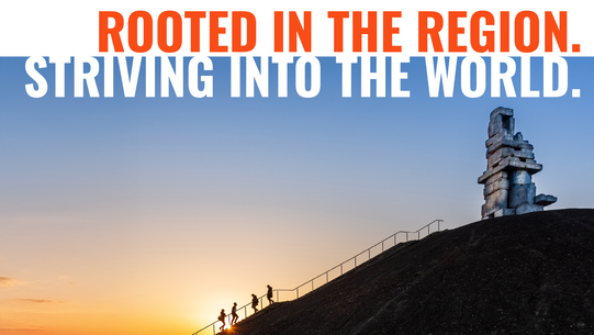 Side view of a slag heap, groups of people climbing up or down a staircase, on the slag heap there is a sculpture made of stones.