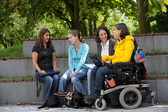 Photo of students on the campus of TU Dortmund University: One of the students is in a wheelchair. Two others are carrying white canes.