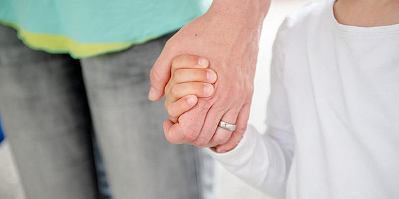 A child's hand holds an adult's hand.