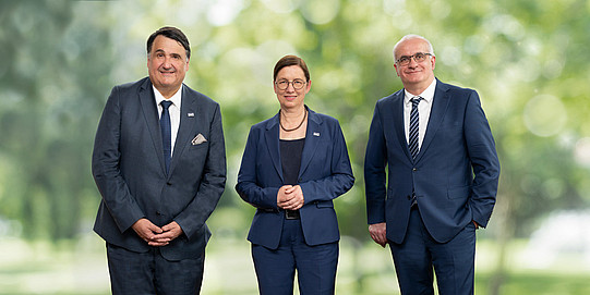 Group photo: A photo of the rectors of the UA Ruhr in front of a blurred green background.