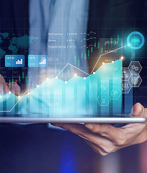 Photo: Two hands holding and operating a tablet. Animated graphs and data can be seen above the tablet.