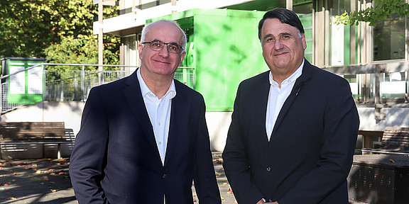 Photo: Prof. Manfred Bayer, President of TU Dortmund University, and Prof. Martin Paul, President of Ruhr University Bochum, stand in front of a green building and smile for the camera.