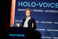 Photo: A person speaks at a podium in front of a blue wall with the words “HOLO-VOICES.”