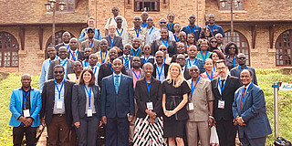 Large group of conference participants poses in front of a building at Uganda Christian University.